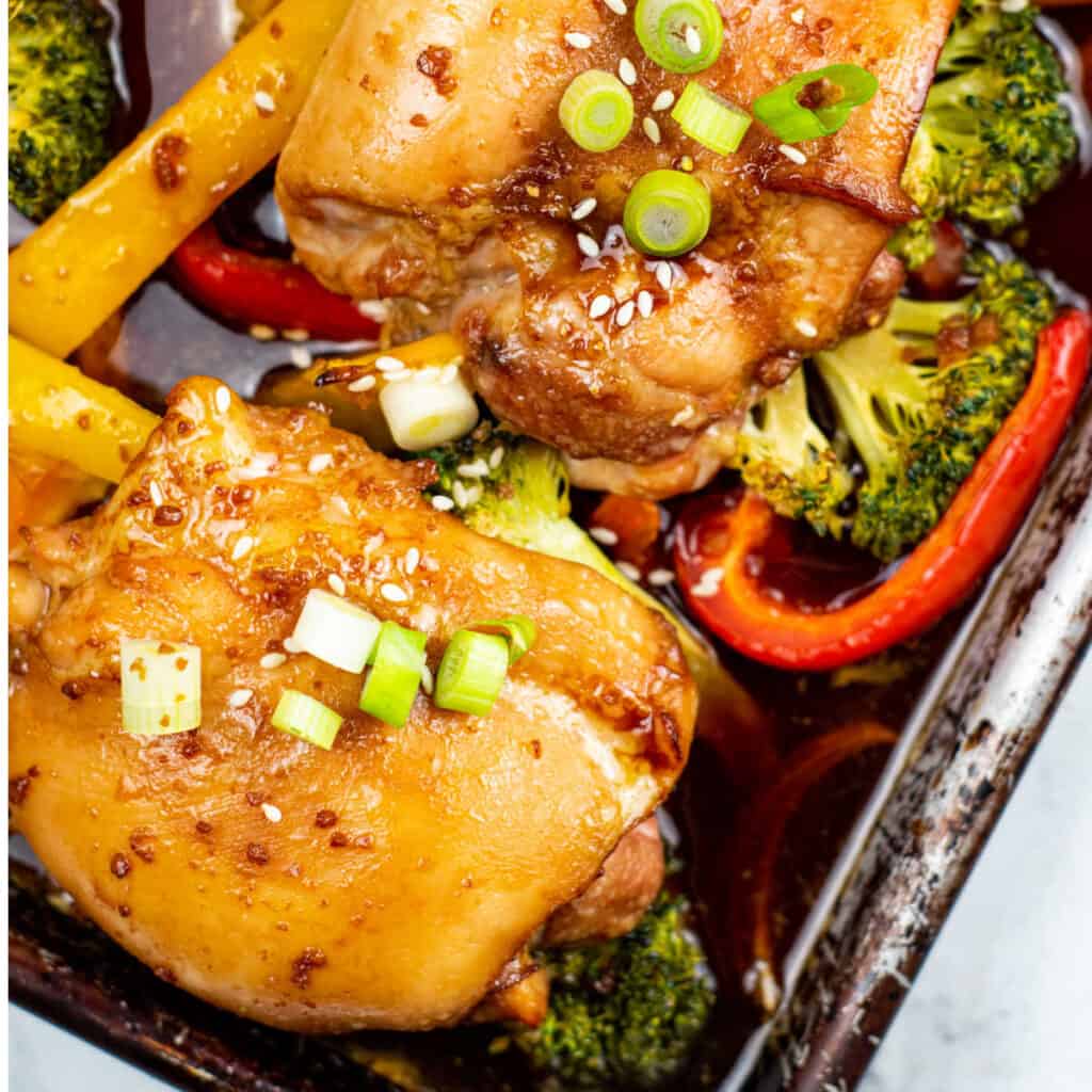 A close-up of a sheet pan of teriyaki chicken and various mixed vegetables.