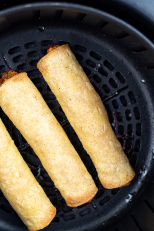 An overhead view of a batch of chicken taquitos in the basket of an air fryer.
