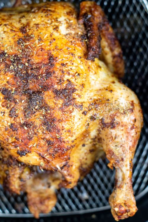 A close up of a roasted chicken in the basket of an air fryer