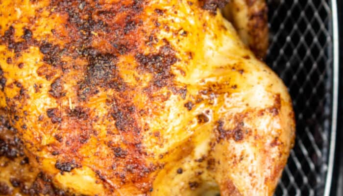 A close up of a golden brown roast chicken in the basket of an air fryer.