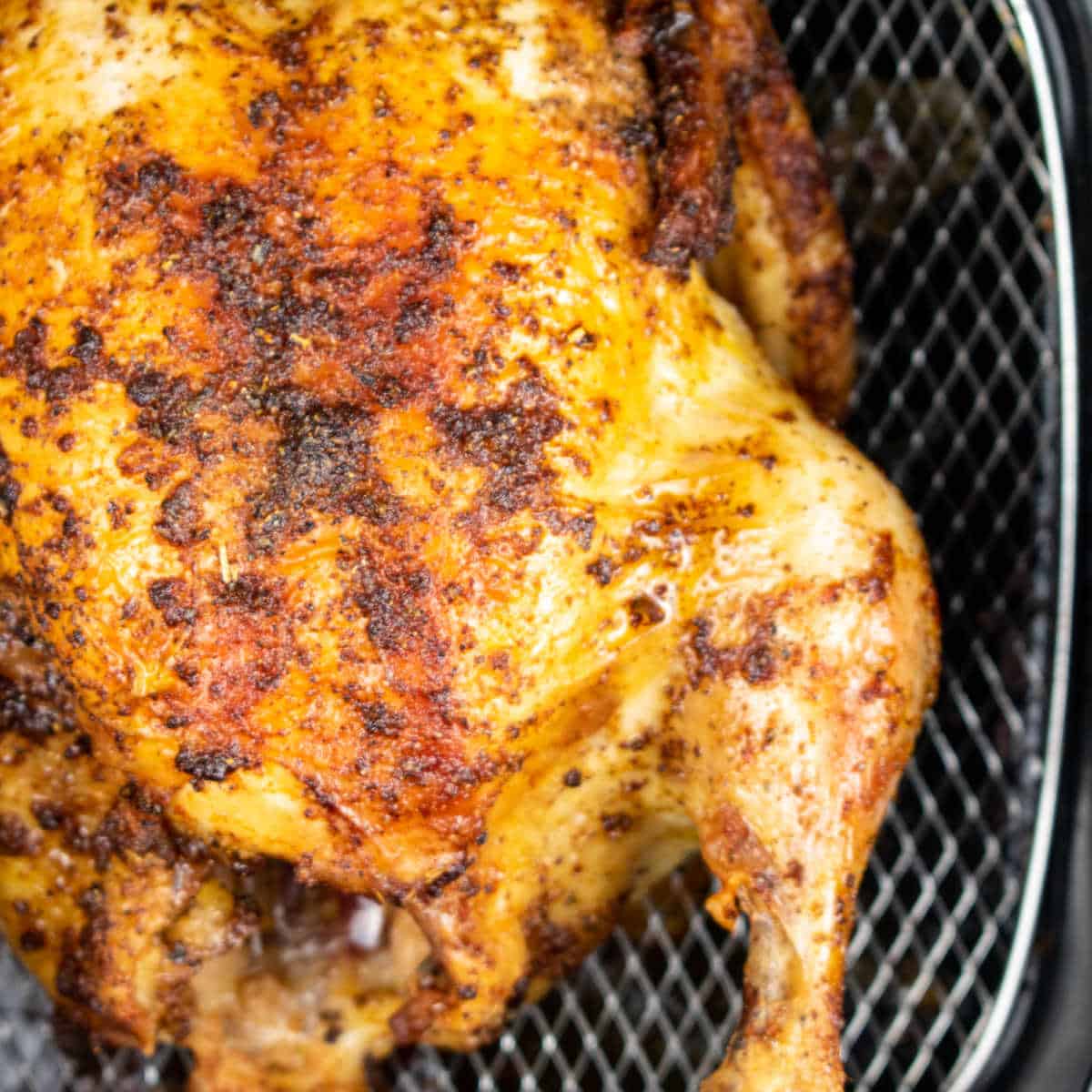 A close up of a golden brown roast chicken in the basket of an air fryer.