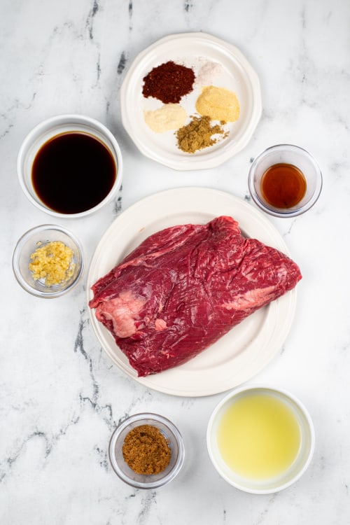 An overhead view of several ingredients for carne ranchero on a marble countertop.