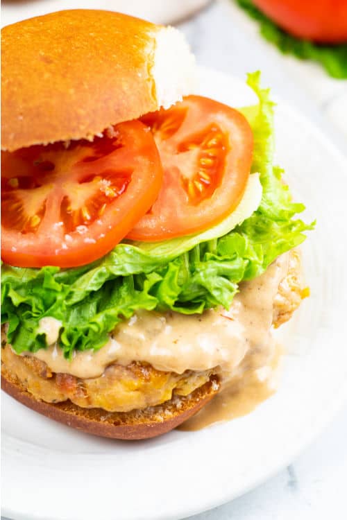 A chicken bacon ranch burger topped with a creamy sauce on a white plate.