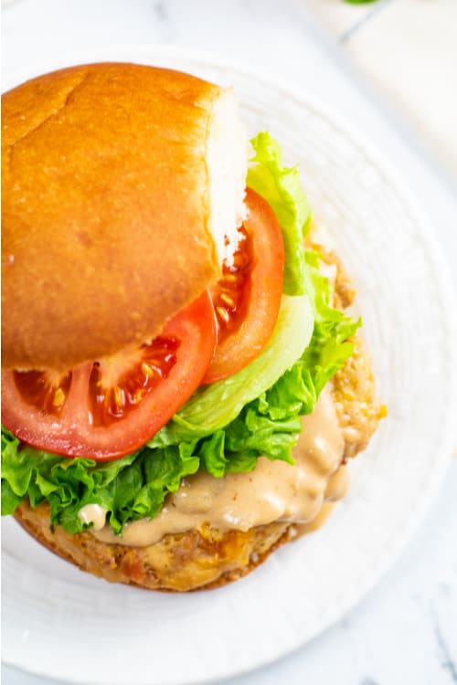 A chicken bacon ranch burger topped with a creamy sauce on a white plate.