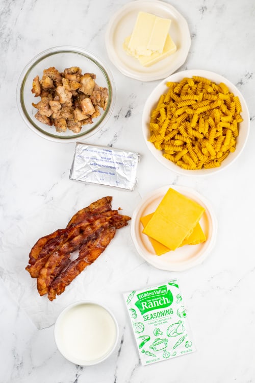 An overhead view of several ingredients for chicken bacon ranch pasta on a marble countertop.