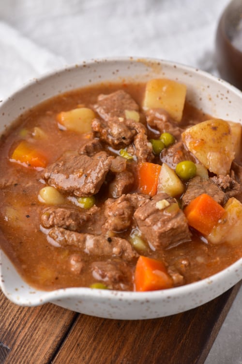 A large white bowl of instant pot vegetable beef soup on a wooden cutting board.