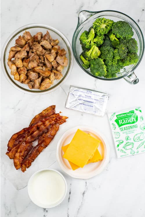 An overhead view of several ingredients for chicken bacon ranch casserole on a marble countertop.