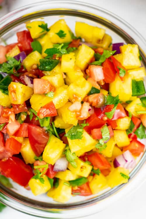 An overhead view of a small glass bowl of pineapple pico de gallo.