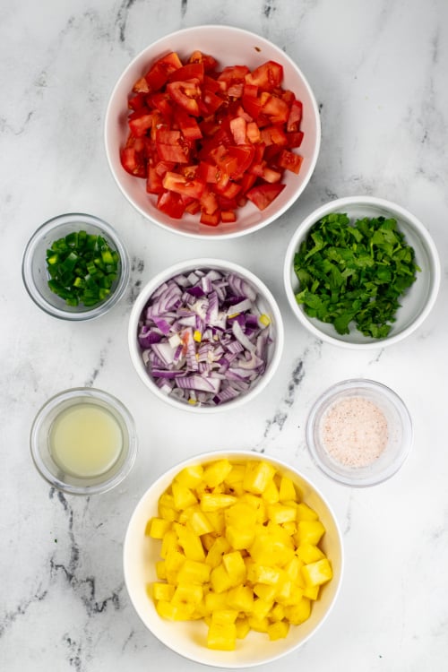 An overhead view of several ingredients for pineapple pico de gallo on a marble countertop.