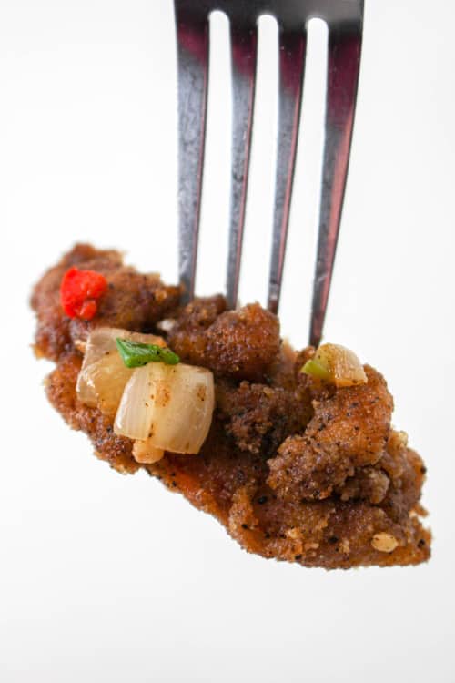 A close-up of a piece of salt and pepper chicken on the end of a fork.