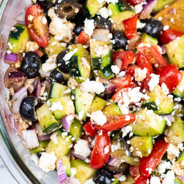 A close-up of a large glass bowl of Mediterranean cucumber salad.
