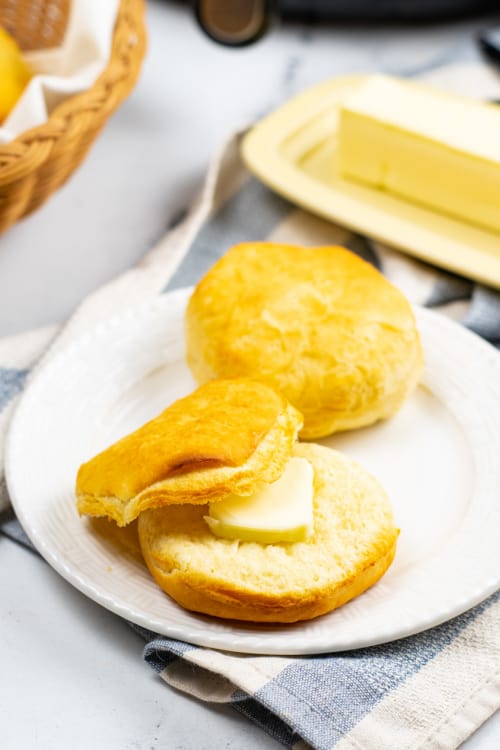 A white plate of buttered air fryer biscuits on a dish towel.