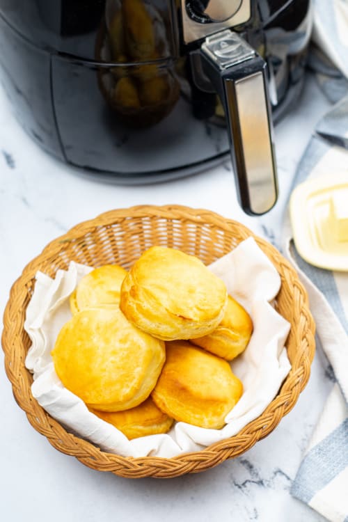 A basket of biscuits on a marble countertop alongside an air fryer.