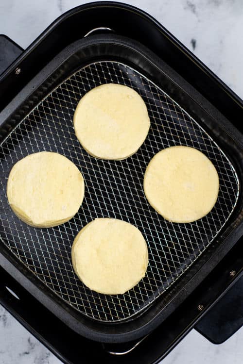An overhead view of four uncooked biscuits in the basket of an air fryer.