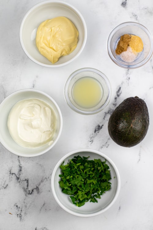 An overhead view of several ingredients for avocado cilantro crema on a marble countertop.