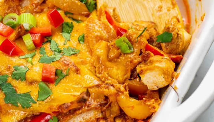 A close-up of a large white dish of chicken fajita casserole being scooped with a wooden spoon.