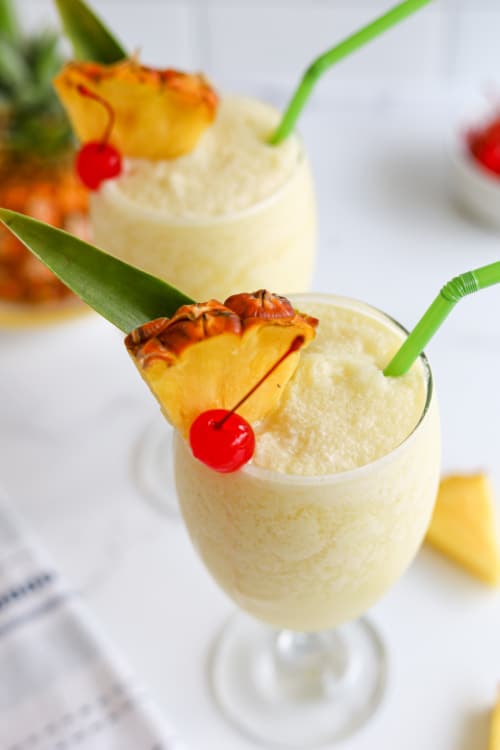 A piña colada mocktail in a glass topped with pineapple and cherry on a marble countertop.