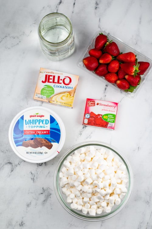 An overhead view of several ingredients for strawberry fluff on a marble countertop.