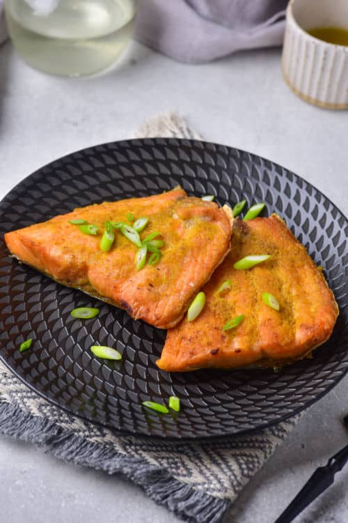 A black plate of air fried salmon topped with green onions.