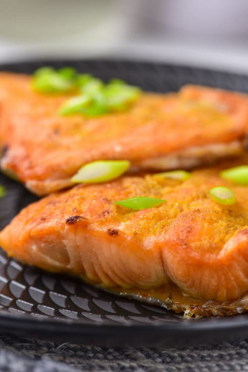 A close-up of a black plate of air fried salmon topped with green onions.