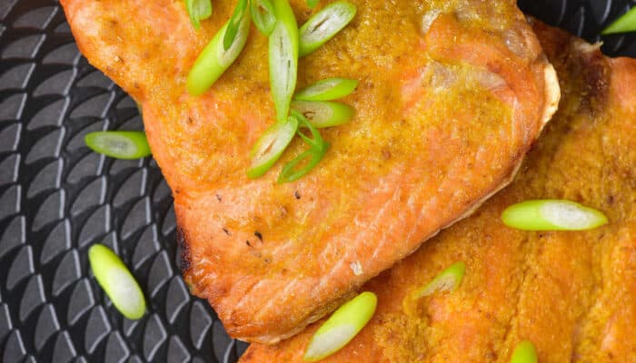 A close-up of a black plate of air fried salmon topped with green onions.