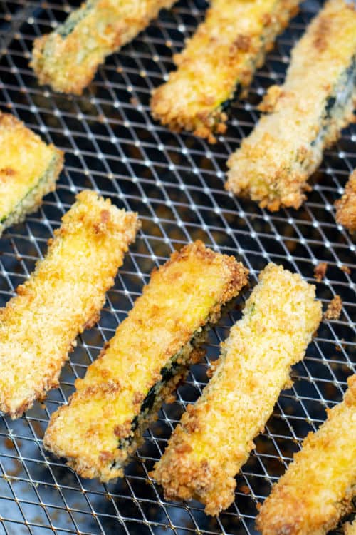 An overhead view of a batch of zucchini fries in an air fryer.