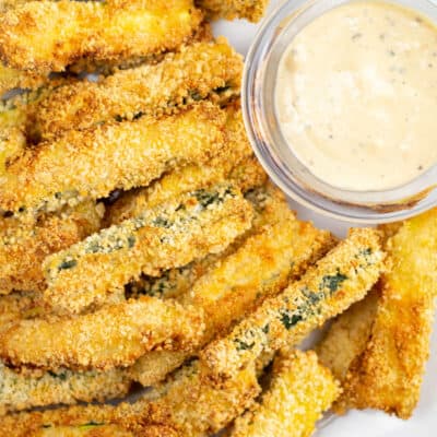 An overhead view of a batch of air fryer zucchini fries along with a small glass dish of dipping sauce.