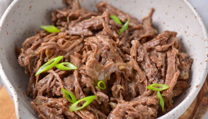 A white bowl of instant pot roast beef and gravy topped with green onions