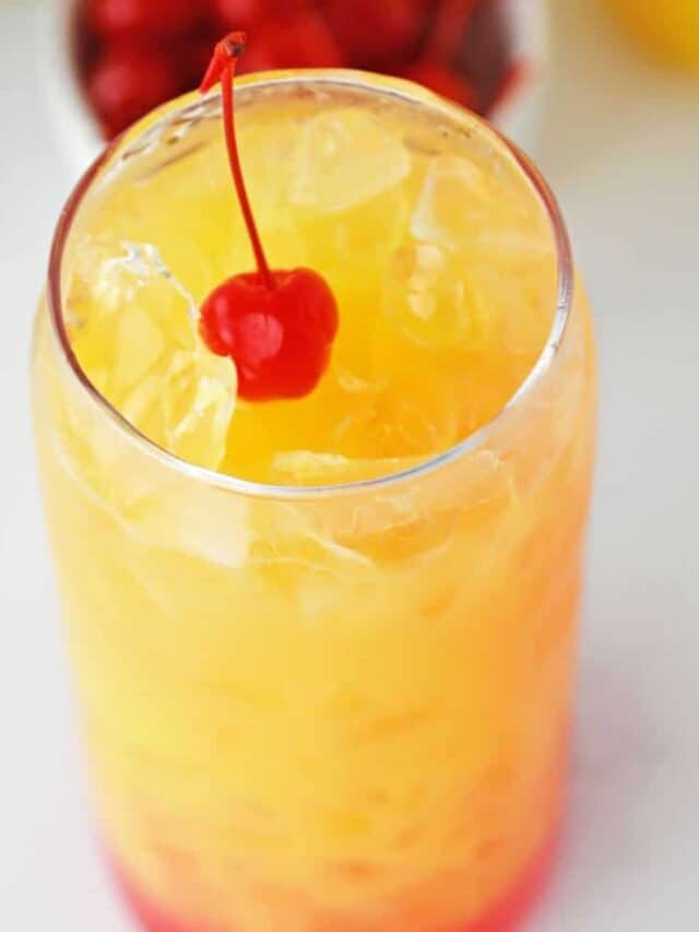 A close-up of a tall glass of malibu rum punch topped with a cherry.