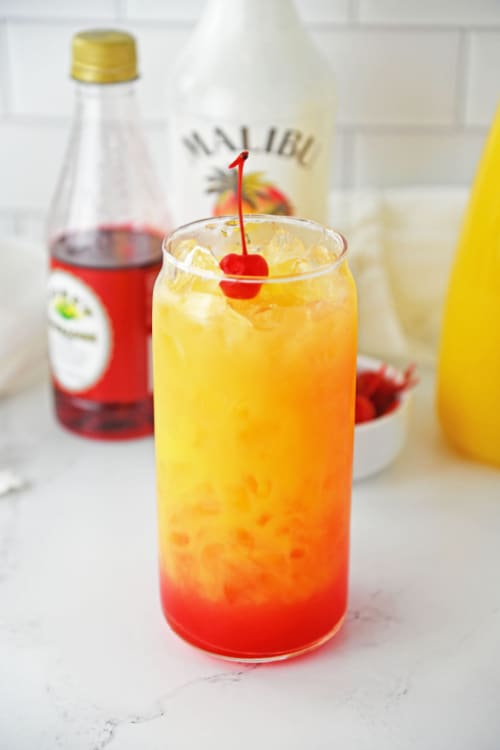A tall glass of Malibu rum punch topped with a cherry.