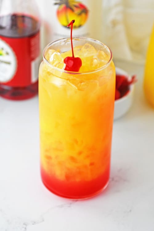 A tall glass of Malibu rum punch topped with a cherry.