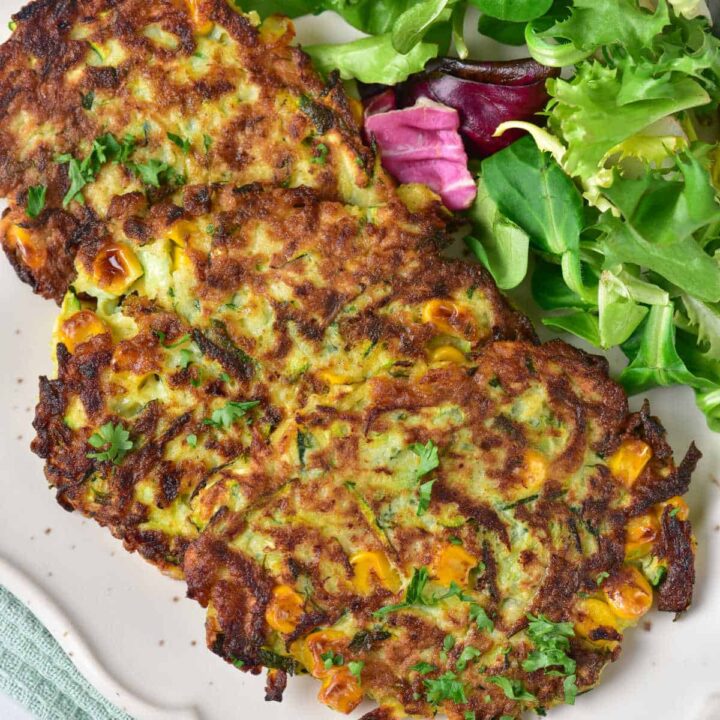 A close-up of a plate of zucchini corn fritters with a small side salad.