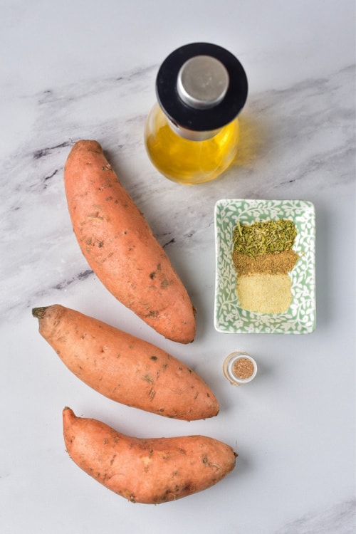 An overhead view of several ingredients for air fryer sweet potato fries on a marble countertop.