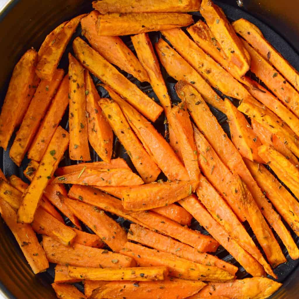 A close-up of a batch of sweet potato fries in the basket of an air fryer.