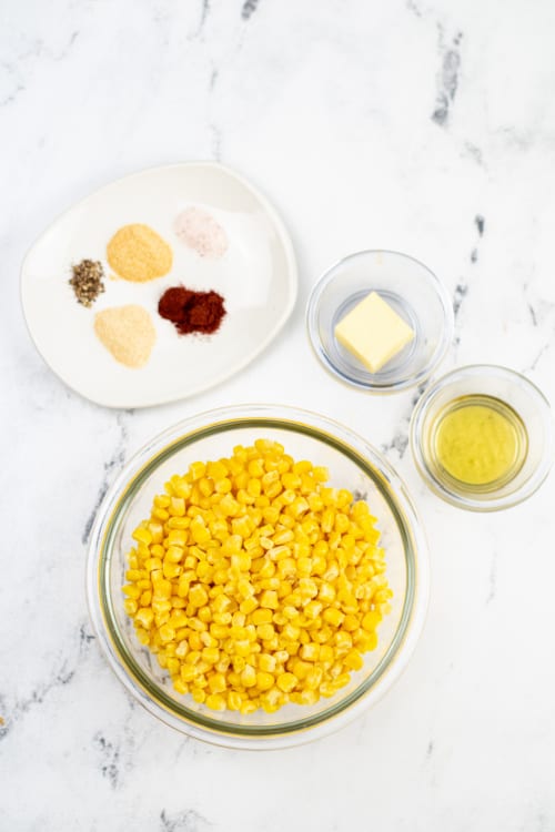 An overhead view of several ingredients for blackened corn on a marble countertop.