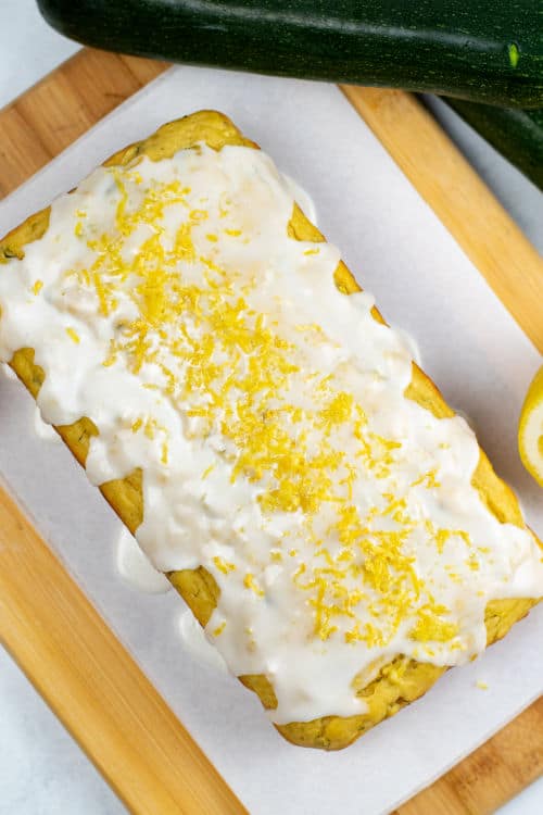 A loaf of lemon zucchini bread covered with glaze and garnished with lemon zest.