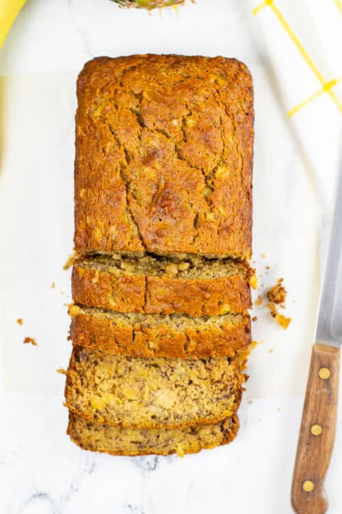 An overhead view of a sliced loaf of pineapple banana bread on a marble countertop.
