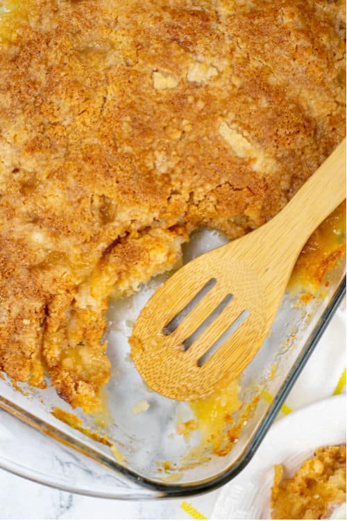 A glass baking pan of pineapple dump cake being scooped with a wooden spoon.