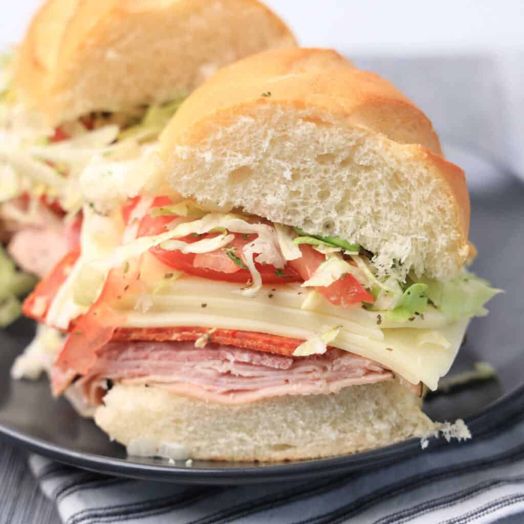 A close-up of an Italian grinder sandwich cut into two halves on a black plate.