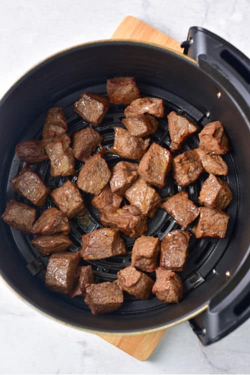 An overhead view of a batch of steak bites in the basket of an air fryer.