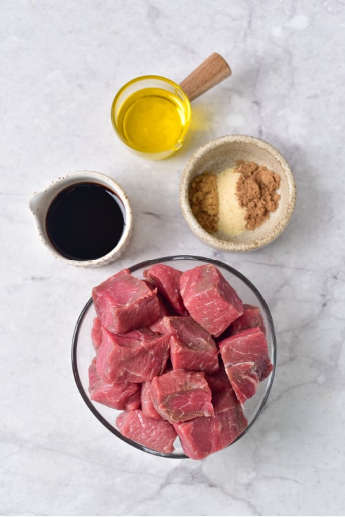 An overhead view of several ingredients for air fryer steak bites on a marble countertop.