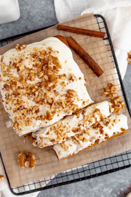 An overhead view of a loaf of pumpkin bread with cream cheese icing cut into slices.