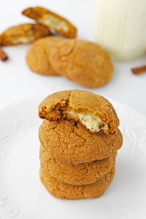 A white plate of several pumpkin cheesecake cookies stacked on top of each other.