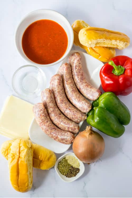 An overhead view of several ingredients for slow cooker Italian sausage sandwiches on a marble countertop.