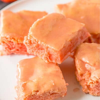 A close-up of a batch of strawberry cake mix brownies on a white plate.
