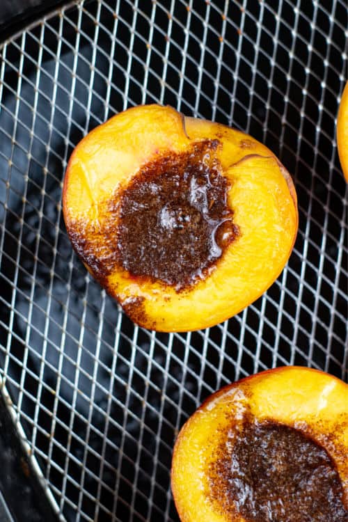 A peach half filled with melted butter and cinnamon sugar in the basket of an air fryer.