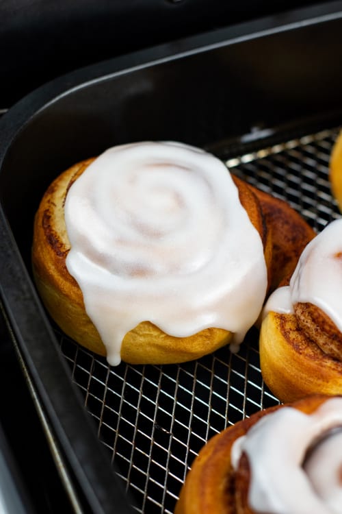 A close up of a cinnamon roll in the basket of an air fryer.