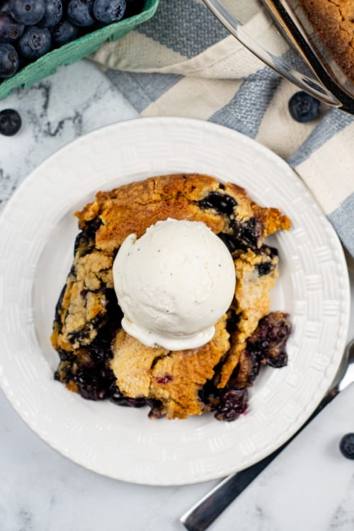 A white plate with blueberry cobbler topped with vanilla ice cream.