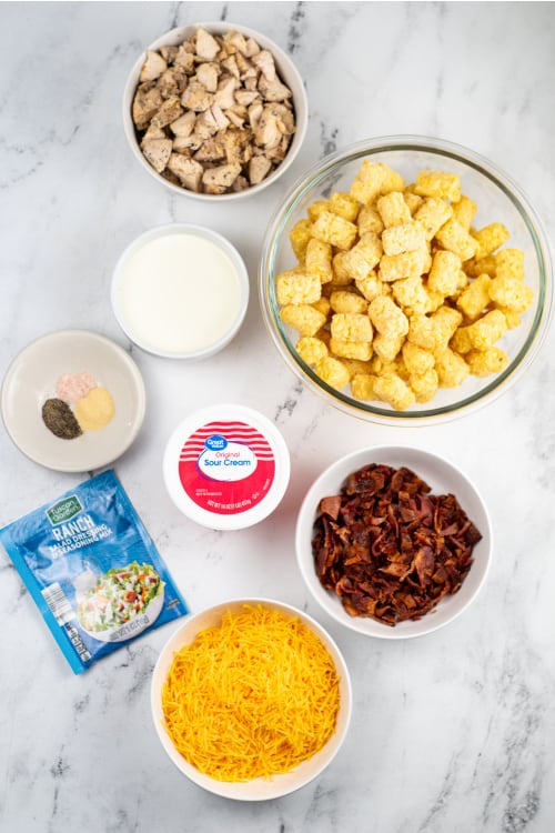 An overhead view of several ingredients for chicken tater tot casserole on a marble countertop.