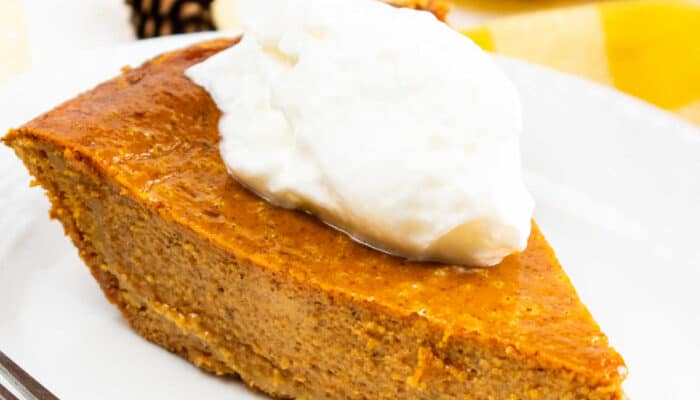 A piece of pumpkin pie with a dollop of whipped cream on a white plate